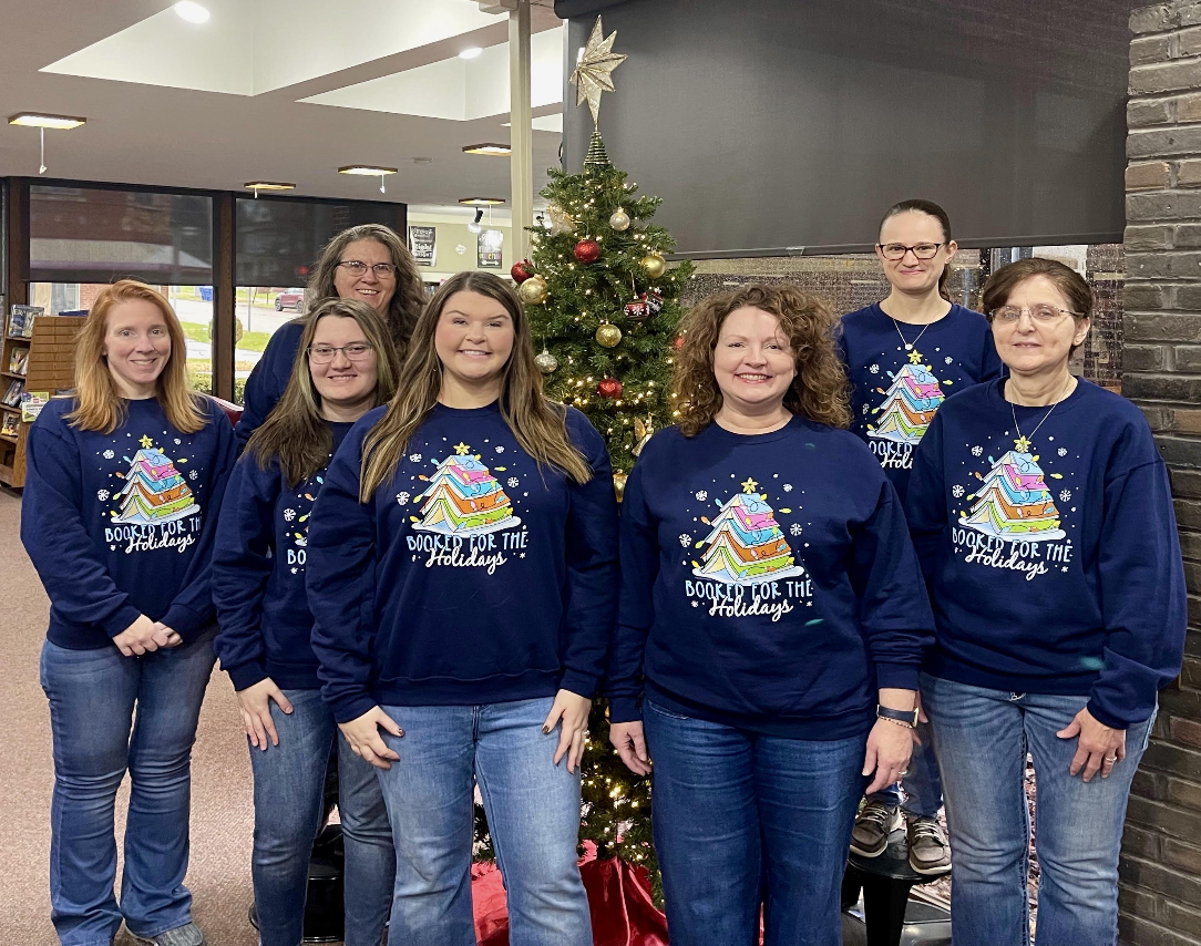 Library staff members in front of the Christmas tree all wearing matching navy sweatshirts